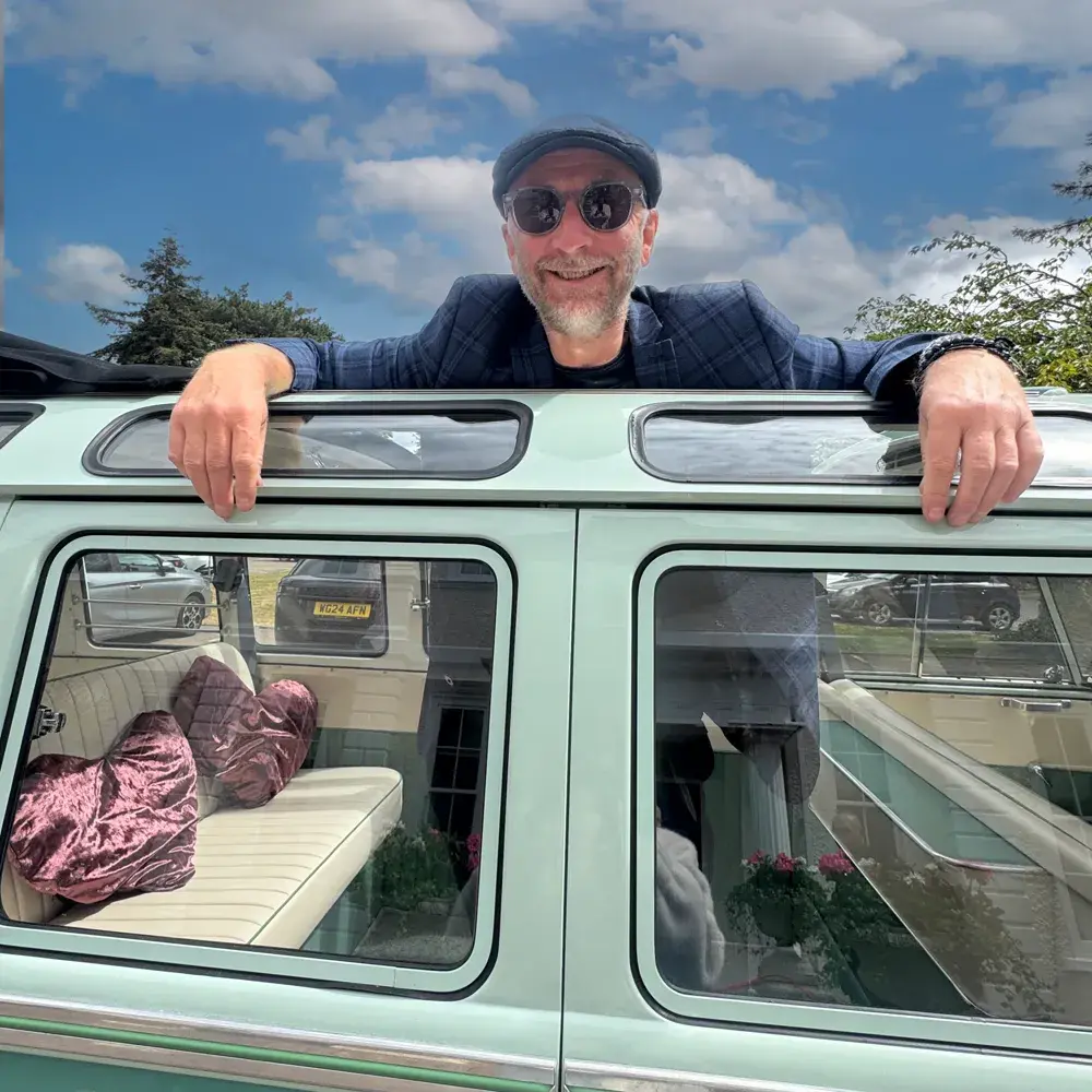 Andy, the owner of Rock The Bus, standing next to Mollie, the vintage VW camper van, in a sunny outdoor setting